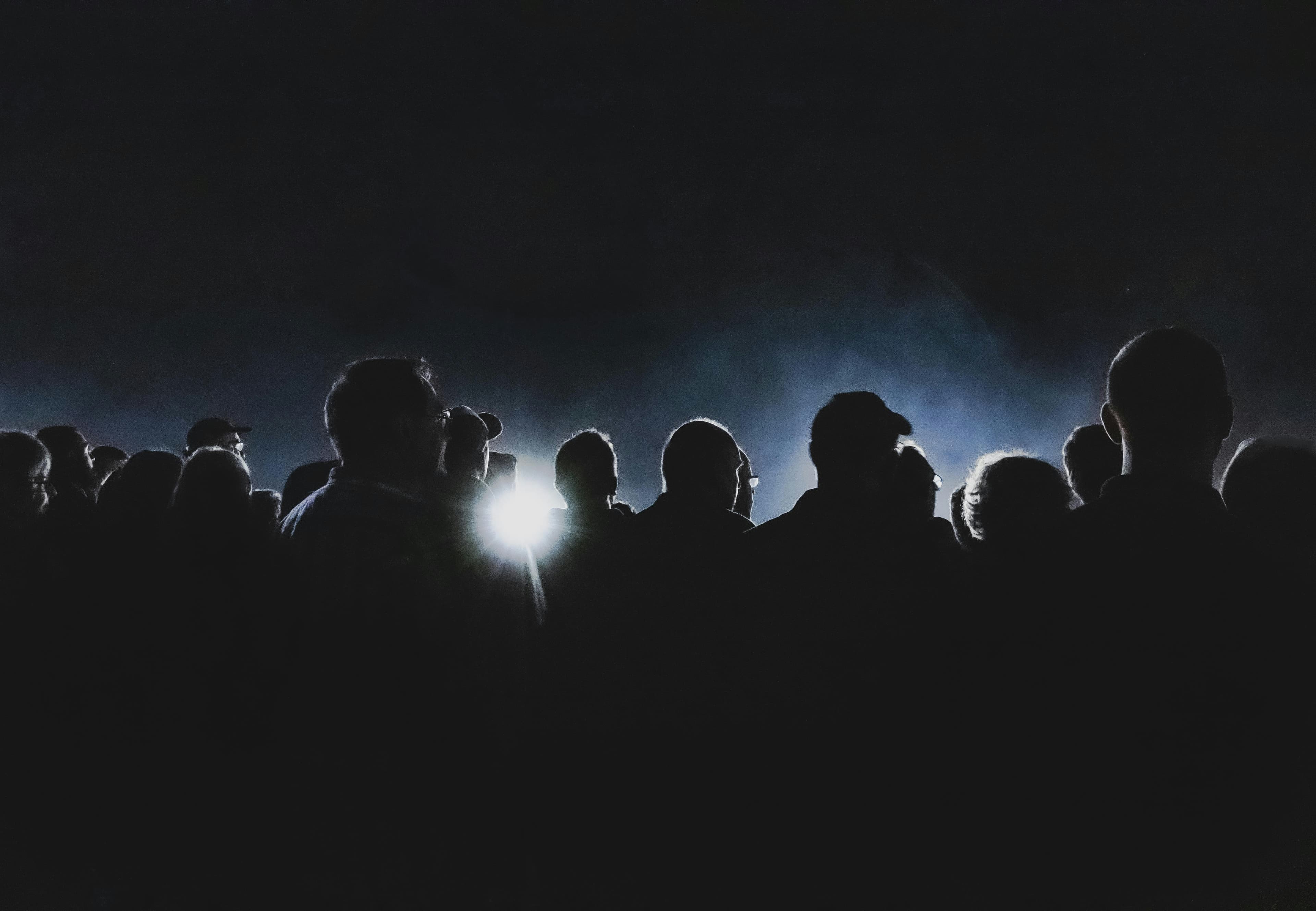 A crowd in near darkness, only a few faces catching the light